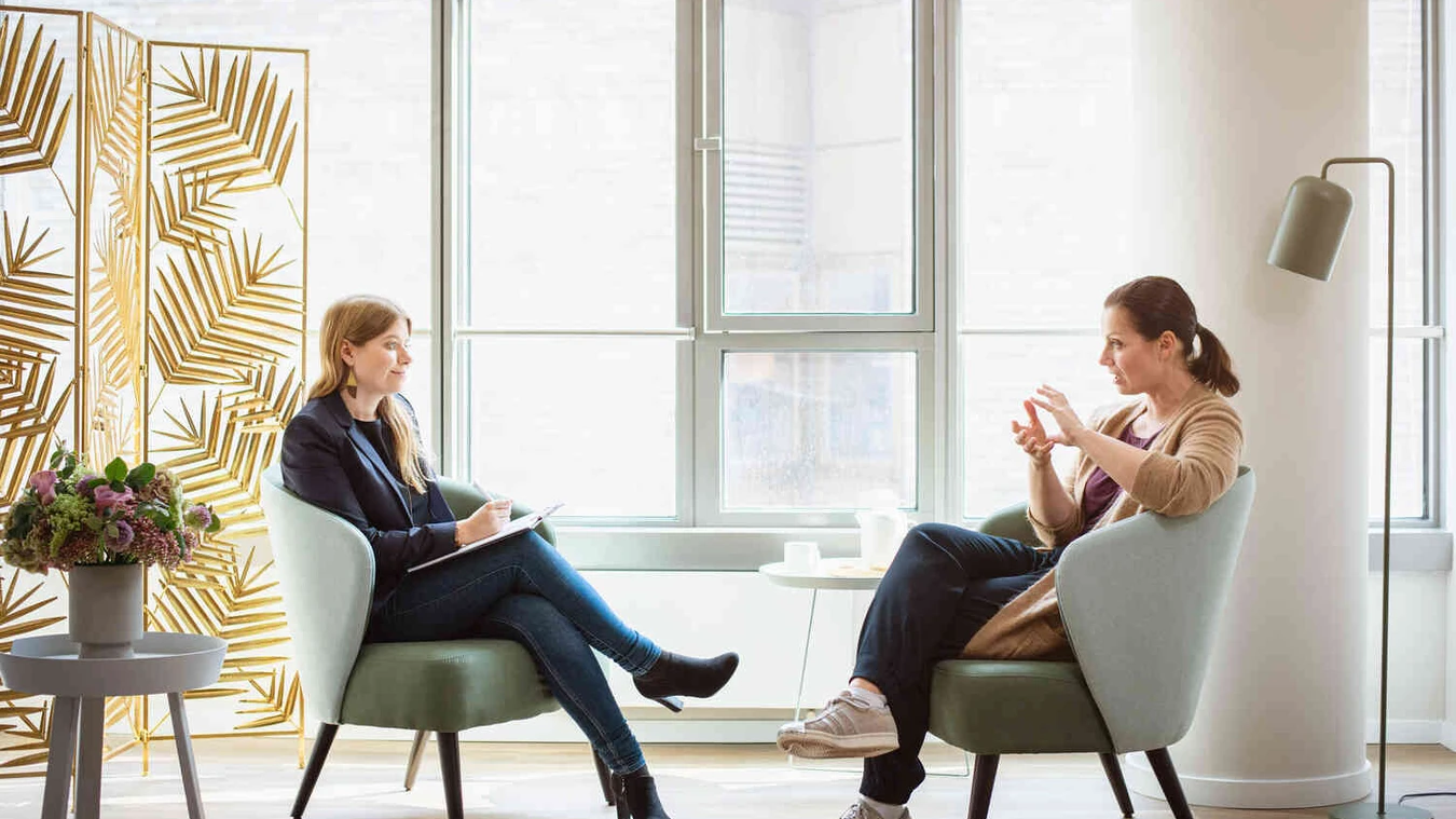 Therapeutin spricht mit Patientin in einem hellen Raum.