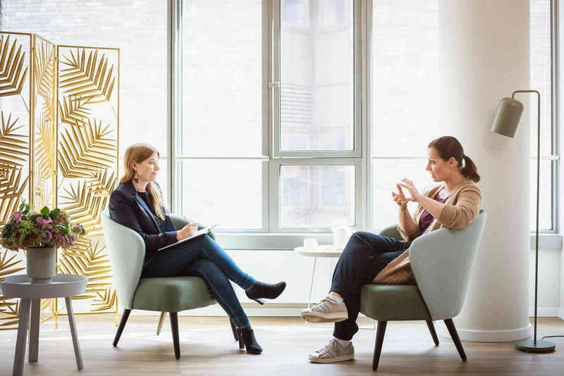 Therapeutin spricht mit Patientin in einem hellen Raum.