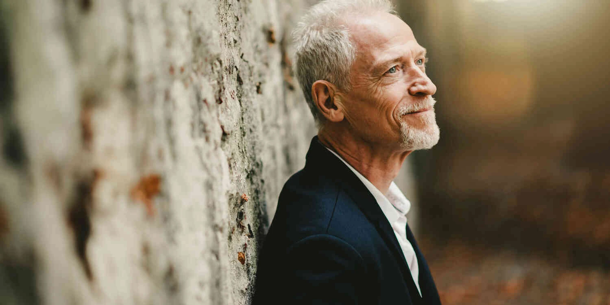 Mann steht angelehnt an einem Baum und l&auml;chelt